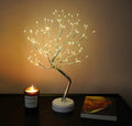 Decorative LED tree on a table with a candle and book in the background